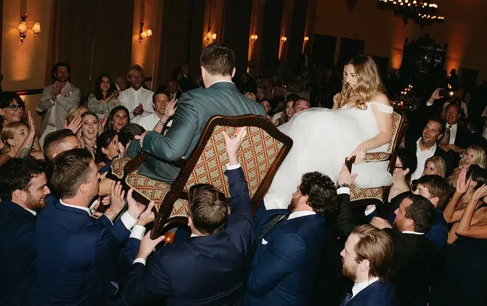 Bride and groom lifted on chairs during the hora as guests celebrate at a ballroom wedding reception