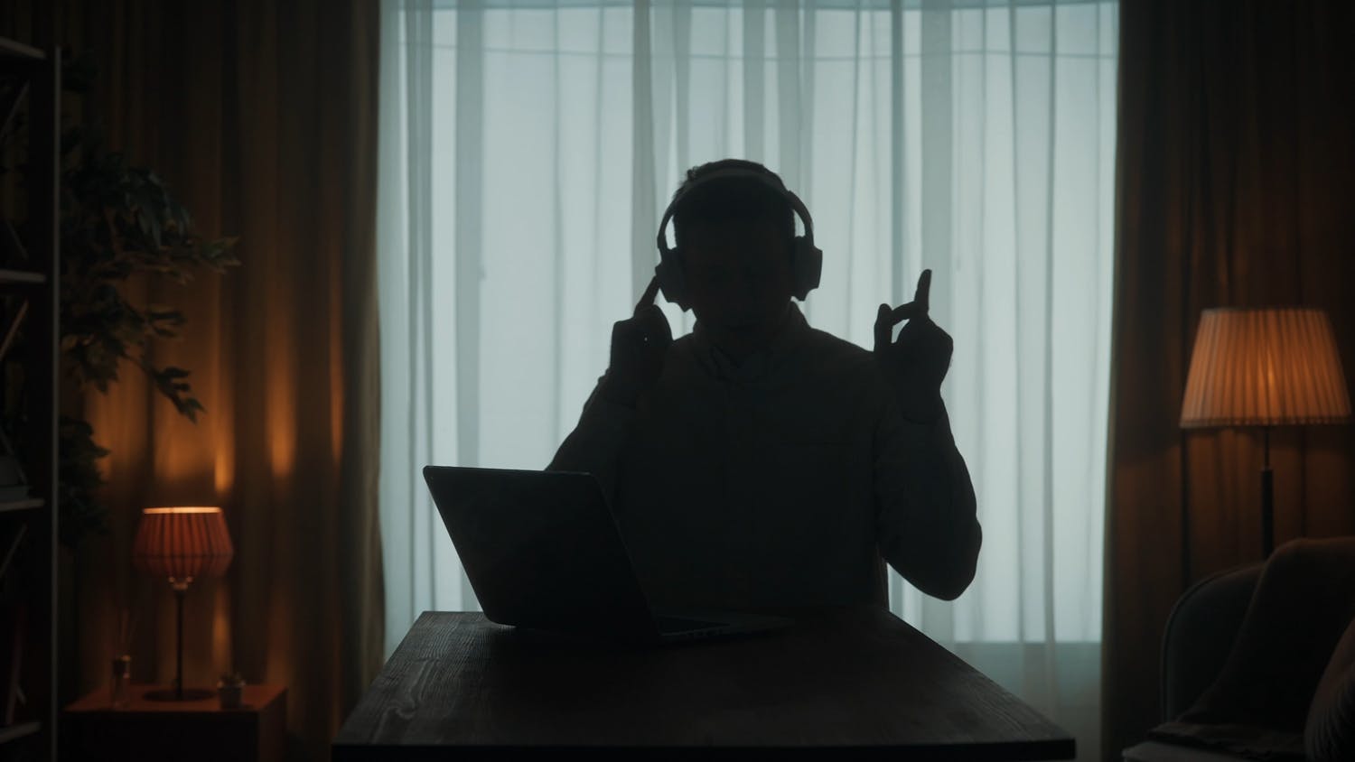 Silhouette of man wearing headphones in front of a laptop